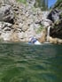 Person in blauem Neoprenanzug und Helm im Wasser nahe eines Wasserfalls.