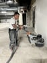 Mann schleift einen Betonboden mit einer großen Schleifmaschine in einem unfertigen Gebäude.