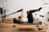 Zwei Frauen trainieren auf Pilates-Reformern mit Schlaufen und Softbällen zwischen den Knien in einem hellen Studio.