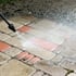 Ein Hochdruckreiniger entfernt tief sitzenden Schmutz von Pflastersteinen. Die Vorher-Nachher Farbveränderung von Braunem Schlamm zu sauberem Rot-Beigen-Pflastersteinen zeigt die Wirksamkeit der Terrassenreinigung.