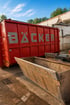 Großer roter Abrollcontainer mit der Aufschrift BÄCKER neben einer metallischen Baggerschaufel auf einem Betriebshof.