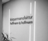Schwarze und weiße Nahaufnahme des Firmenlogos "körpermanufaktur hoffmann & hoffmann" an einer Wand.