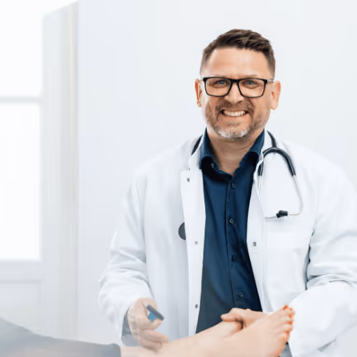 Dr. Csaba Losonc mit Brille und Stethoskop untersucht den Fuß eines Patienten mit einem Reflexhammer.