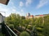Blick vom Balkon auf einen begrünten Innenhof mit vielen Bäumen vor mehrstöckigen Wohngebäuden unter blauem Himmel.