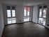 Leeres Zimmer mit dunklem Holzboden, weißen Wänden und drei großen Fenstern mit Blick nach draußen.