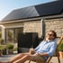 Mann entspannt im Liegestuhl vor einer Wärmepumpe und einem Haus mit Solardach.