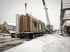 Kran hebt vorgefertigte Hauswandmodule von einem LKW auf einer schneebedeckten Baustelle.