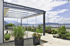 Moderne Glas-Terrassenüberdachung mit Schiebewänden auf einer Holzterrasse mit Pflanzen und Seeblick.