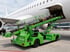Förderung für elektrische Gepäckförderer am Flughafen: grüner Elektro-Belt-Loader belädt ein Flugzeug mit Gepäck