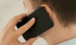 Mann hält schwarzes Smartphone ans Ohr und telefoniert.