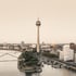 Rheinturm und MedienHafen in Düsseldorf bei Sonnenuntergang mit Booten und Gebäuden.