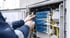 Techniker verbindet Glasfaserkabel in einem geöffneten Verteilerkasten mit blauen Anschlüssen und gelben Kabeln.