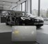 Silberne Kreditkarte mit Kontaktlos-Symbol, John Doe, 4123 5667 801 2345, vor schwarzem Tesla im Showroom.