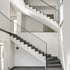 Moderne Steintreppe mit dunklen Stufen und filigranem schwarzen Metallgeländer in einem hellen, minimalistischen Treppenhaus.