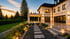 Luxuriöses Haus mit beleuchteter Terrasse und Gartenweg bei Sonnenuntergang.