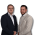 Zwei lächelnde Männer in Anzügen, der eine in Dunkelblau, der andere in Beige, stehen nebeneinander.