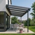 Moderne Pergola mit Lamellendach über einer Terrasse mit Esstisch und Stühlen neben einem Haus.