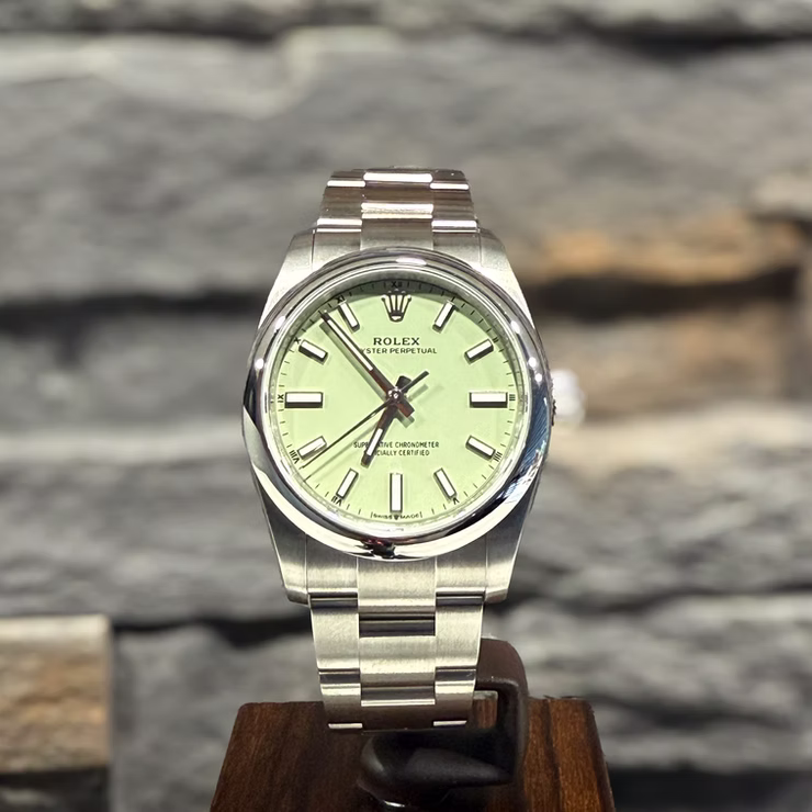 Silberne Rolex Oyster Perpetual Uhr mit hellgrünem Zifferblatt auf Holzständer vor Steinwand.