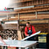 Handwerker der Firma Dippe bearbeitet weiße Platten in einer Holzwerkstatt neben Brennholz und einer gelben Tonne.