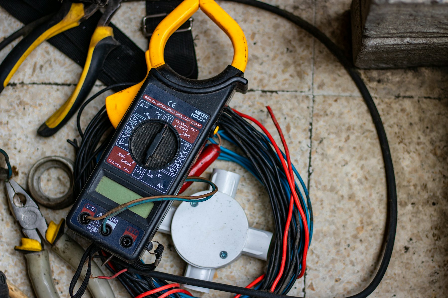An electrician in gloves holding a multimeter probe to the terminals of an opened residential EV charger enclosure in a garage