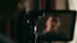 Close-up of a studio microphone with a blurred reflection of a person on a screen in the background.