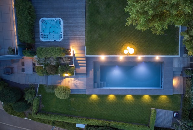 Beleuchtete Poolanlage mit Überlaufrinne und Whirlpool von oben bei Nacht