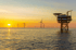 Meer mit Sonnenuntergang, Windkraftanlagen und einer Offshore-Plattform.