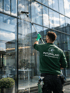 Ein Mann in grüner "Putzpalast Reinigungsservice" Uniform reinigt ein großes Glasfenster mit einer Teleskopbürste.
