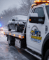 Towing Port Charlotte winter recovery service transporting a disabled car on a flatbed tow truck during snowfall.