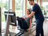 A clinical provider in blue scrubs assists a woman using a leg press machine in a bright rehabilitation clinic.