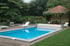 Ein blaues Schwimmbecken mit weißer Poolabdeckung, Liegestühlen und einem Gartenpavillon inmitten einer grünen Gartenanlage.