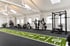 Moderner Fitnessraum mit Kraftgeräten, Rack, Hantelbank und einer grünen Kunstrasen-Sprintbahn mit Ziffernmarkierung.