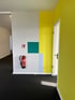 Roter Feuerlöscher an einer weißen Wand mit gelben, türkisen und hellblauen Farbflächen.