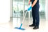 Person in blauer Uniform und Handschuhen wischt einen Fliesenboden mit einem blauen Mopp.