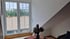 Ein Dachzimmer mit einem großen Fenster, das auf ein Dach und Bäume blickt, mit einem Tisch und einer Vase.