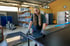 Eine junge Mitarbeiterin mit Schutzhandschuhen bearbeitet eine Metallplatte an einem Werktisch in einer Industriehalle.