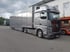 Grauer Mercedes-Benz LKW mit langem Anhänger parkt auf Asphaltfläche, Gebäude im Hintergrund.