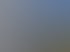Eine graue Gelenkarmmarkise ist an einem weißen Haus über einer Terrasse ausgefahren.