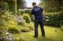 Ein Gärtner in einem dunkelblauen HSK-Shirt trimmt Gras mit einem Freischneider in einem blühenden Garten.