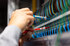 Hände prüfen bunte Elektrokabel mit Multimeter-Sonden in einem Serverschrank.