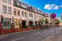 Modernes, weißes Eckgebäude mit vielen Fenstern und einer gläsernen Rundung, daneben eine Straße und blauem Himmel.