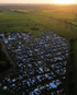 Luftaufnahme eines großen Campingplatzes mit vielen Zelten und Autos neben grünen Feldern bei Sonnenuntergang.