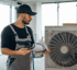 Techniker in Arbeitskleidung und Kappe prüft Papiere neben einer großen Klimaanlage mit Ventilator.