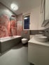 Modernes Badezimmer mit Badewanne, floraler Motivwand in Rosa-Grau, Hänge-WC und weißem Doppelwaschtisch.