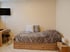 Ein Bett mit gemusterter Decke und Kissen, an der Wand ein Fernseher, daneben ein Schreibtisch und Stuhl.