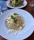 Teller Spaghetti Carbonara mit Parmesan und Petersilie, dahinter ein Salat und ein Wasserglas.