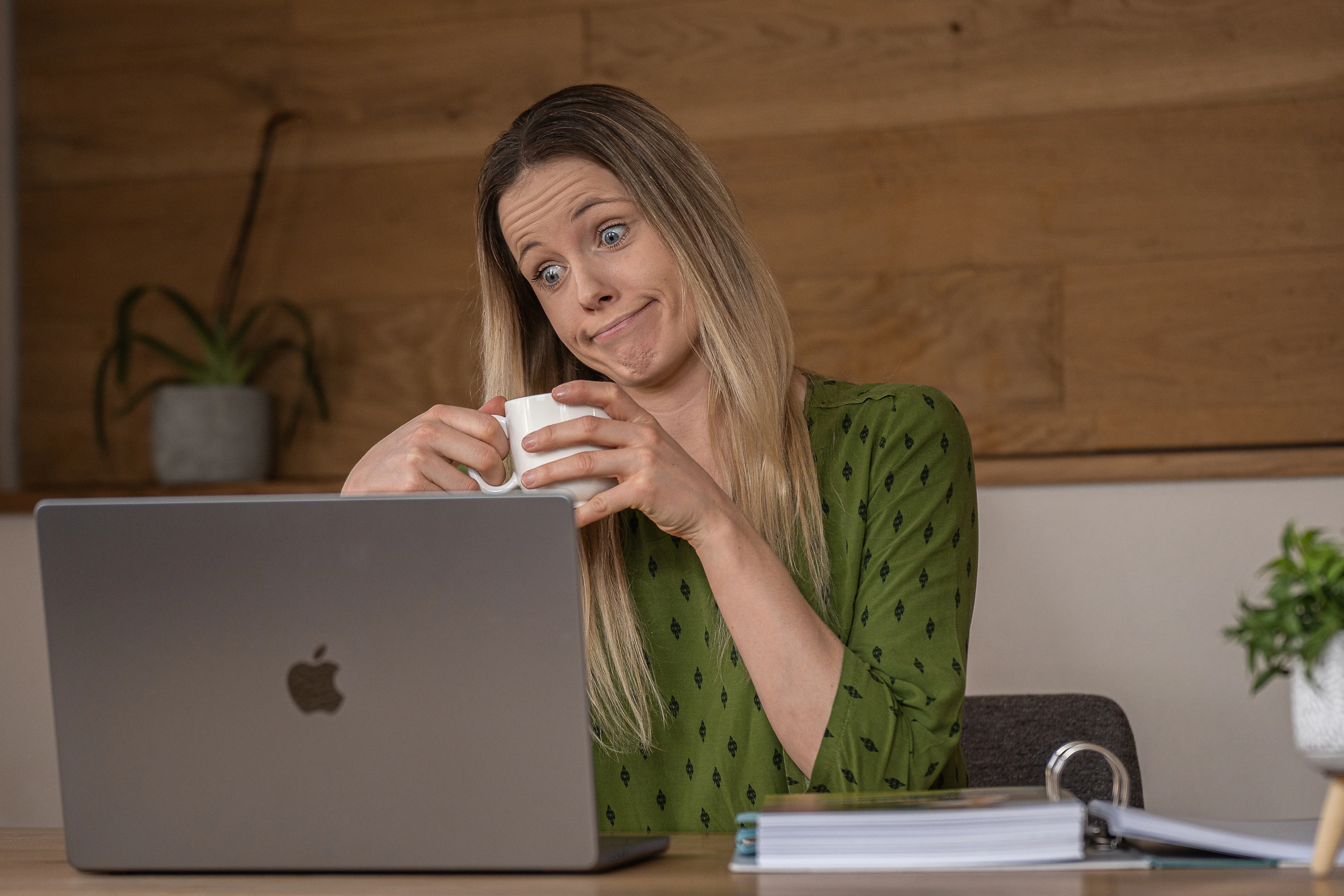 Sabrina sitzt mit einer Tasse am Laptop und schaut zweifelnd