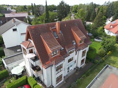 Luftaufnahme eines dreistöckigen weißen Hauses mit rotem Ziegeldach, Balkonen und einem Garten.