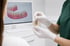 Zahnarzt zeigt einer Patientin ein Zahnimplantat-Modell vor einem Monitor mit digitalem Gebiss.