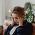 Woman in dark blue pajamas holding her head, looking down, showing signs of brain fog.